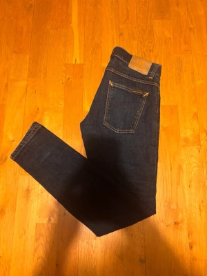 Mörkblå Nudie jeans - Snygga, nästan nya mörkblå jeans från Nudie. Klassisk femficksdesign med kontrastsömmar och läderpatch bak i midjan. Jeansen är tillverkade i ett mjukt och stretchigt denimtyg som sitter skönt hela dagen.