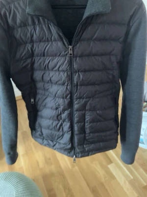 Mörkgrå quiltad cardiganjacka - Snygg mörkgrå cardiganjacka med quiltad front och mjuka stickade ärmar och rygg. Jackan har dragkedja framtill, hög krage och praktiska fickor. Perfekt för lager-på-lager och en stilren look.