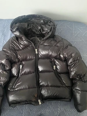 Zara puffer - Tja, Säljer en svart/brun, glansig pufferjacka från Zara med stor huva och två snedställda dragkedjefickor framtill. Jätte bra skick nästan som ny, inga defekter. Jackan har en rejäl vaddering och breda kanaler som ger en riktigt puffig look. Storlek S, nypris 1200 säljer för 699kr Den är riktigt skön att ha på sig samt att den håller värme bra. Hör av dig vid fler frågor ✌️