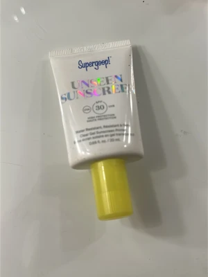 Supergoop! Unseen Sunscreen SPF 30 - Transparent solskyddsgel från Supergoop! med SPF 30. Tuben är vit med holografisk text och har ett gult lock. Produkten är vattenresistent och passar perfekt för dagligt skydd mot solen.