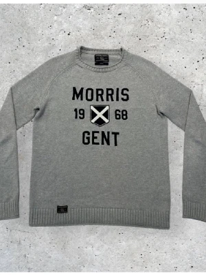 Grå tröja från Morris Gent - Snygg grå tröja från Morris Gent med svart text och ett skotskt inspirerat emblem på bröstet. Tröjan har rund halsringning, långa ärmar och ribbade muddar vid ärmslut och nederkant. Perfekt för en stilren och avslappnad look.