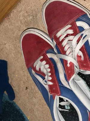 Vans Old Skool blå/röd sneakers - Klassiska Vans Old Skool sneakers i blått och rött med vit sula och vita skosnören. Skorna har den ikoniska vita sidan och är tillverkade i mocka och canvas. Perfekta för dig som gillar streetwear och vill ha en färgstark look.