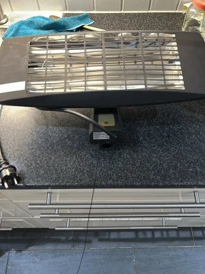 Svart elektrisk värmare med sladd - Elektrisk värmare i svart metall med galler framtill och strömbrytare i mässing. Utrustad med sladd och stickkontakt, perfekt för att värma upp mindre utrymmen. Modern och stilren design som passar i de flesta miljöer.