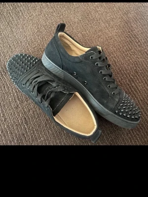 Svarta sneakers med nitar - Snygga svarta sneakers i mockaimitation med svarta nitar på tån och svarta skosnören. Skorna har en låg profil och svart sula. Perfekta för dig som vill sticka ut med en edgy stil och grisch