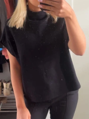 Svart polotopp i bomull - Säljer en svart polotopp med korta ärmar och avslappnad passform. Toppen har en hög krage och är gjord i mjuk bomull, perfekt för en clean och enkel stil. Passar till allt och är lätt att matcha med olika outfits.