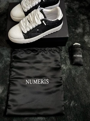 Numeris Sneakers - Säljer ett par stilrena sneakers från Numeris i svart och vitt. Skorna har en chunky vit sula, grova vita skosnören och ovandel i svart tyg med slitna detaljer. Tå och häl är i vitt läderliknande material. Kommer med dustbag och förpackning.