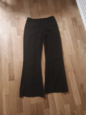 Svarta utsvängda kostymbyxor - Snygga svarta kostymbyxor med hög midja och utsvängda ben. Byxorna har pressveck framtill för en clean look och är sydda i ett mjukt, följsamt tyg som ger en skön passform. Perfekta för dig som gillar en stilren och trendig vibe.