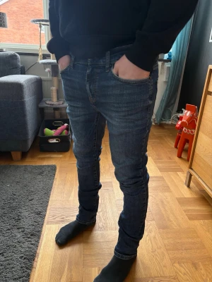 Mörkblå Jeans - Snygga mörkblå jeans i modellen slim fit med smal passform och lätt avsmalnande ben. Klassisk 5-ficksmodell med normalhög midja. Fin mörk tvätt med diskreta slitningar/fade-effekt framtill som ger en stilren look.  Storlek: W28 L32 Skick: Bra skick, inga hål eller fläckar Passar perfekt både till vardag och mer uppklätt med skjorta eller kavaj.  Säljes då de inte längre kommer till användning. 🌿