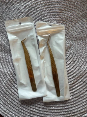 Guldiga pincetter för fransförlängning - Två guldiga pincetter med sned spets, perfekta för fransförlängning eller detaljarbete. De har ett räfflat grepp för bättre kontroll och är tillverkade i metall. Kommer i förslutningsbara plastpåsar.