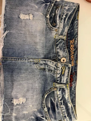 Blå jeanskjol från Terranova - Cool kort jeanskjol från Terranova med slitna detaljer och rå fransig nederkant. Kjolen har klassiska fickor fram och bak, samt knapp och dragkedja. Sitter som en M/ S