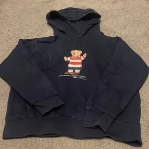 Mörkblå hoodie från Ralph Lauren med björnmotiv - Säljer en mörkblå hoodie från Ralph Lauren med ett björnmotiv på framsidan. Tröjan har långa ärmar och en klassisk huva.