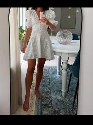 Adoore Sicily klänning strl S - Fint skick.Söt vit kortklänning med puffärmar och v-ringning. Klänningen har fina spetsdetaljer och markerad midja som ger en feminin siluett. Perfekt för sommarens alla tillfällen.