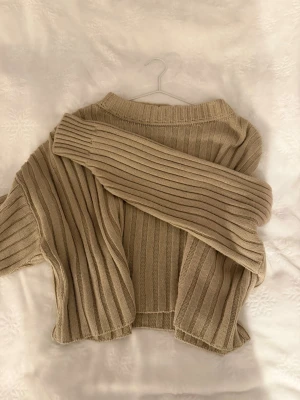 Beige ribbstickad tröja - Säljer en beige ribbstickad tröja med breda ränder och rund hals. Tröjan har långa ärmar och är gjord i ett mjukt stickat material.
