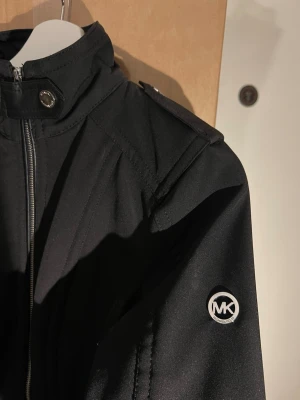 Kappa Michael Kors - Kort kappa i softshell, med detaljer i konstläder, från Michael Kors. Helt ny.