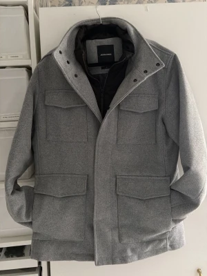 Grå rock från Jack & Jones - Snygg grå rock från Jack & Jones, andvänd en vinter inga defekter. Köpt för 3000 kr