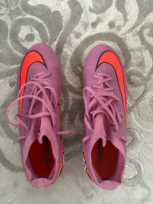 Nike air zoom mercurial vapor 16 PRO - Säljer ett par snygga fotbollsskor från Nike i lila med en stor neonröd swoosh på ovansidan. Skorna har klassisk snörning och är tillverkade i syntetmaterial för bra passform och kontroll på planen. Perfekta för dig som vill sticka ut på matchen!