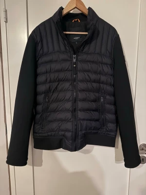 Svart quiltad cardiganjacka - Snygg svart cardiganjacka från märket RockandBlue med quiltad front och rygg samt släta ärmar. Jackan har dragkedja framtill, två fickor med dragkedja och en hög krage. Perfekt för lager-på-lager och stilren look.