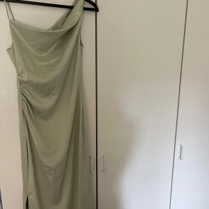 Ljusgrön långklänning från Adoore - Snygg ljusgrön långklänning från Adoore med asymmetrisk axel och smala axelband. Klänningen har draperad effekt på ena sidan och en liten slits nertill. Materialet är glansigt och känns lyxigt! Klänningen är aldrig använd 💚 Passar perfekt till bal eller ett bröllop i sommar🫶🏼