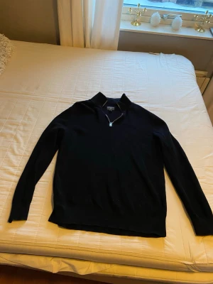 Svart stickad tröja med half sip - Svart stickad tröja med hög krage och half sip framtill. Tröjan har lång ärm och en enkel, stilren design som passar till det mesta. Materialet ser mjukt och bekvämt ut, perfekt för kyligare dagar.