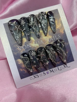 DarkNova (M);Long Stiletto - Unika handgjorda press-on naglar i svart med silverdetaljer, stjärnor och kedjor. Långa och stiletto med handmålade 3D mönster och små pärlor för extra edge. Perfekt för dig som vill sticka ut med en galaktisk och mystisk look.M: 16 mm, 12 mm, 12,5 mm, 11,5 mm, 10 mm