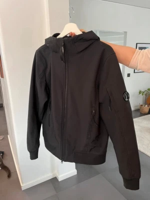 C.P Company jacka  - Svart C.P shell jacka med luva i storlek 48. Fickor med dragkedja. C.P-märket på vänster arm har några små repor, se bild 7. I övrigt fin.