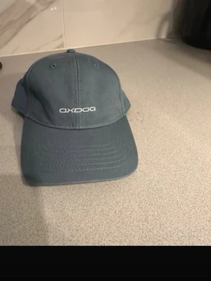 Blå keps från Oxdog med justerbar rem - Snygg blå keps från Oxdog med klassisk böjd skärm och vit logotyp framtill. Kepsen har justerbar rem med metallspänne baktill för perfekt passform. Materialet är slitstark bomull och designen är enkel och stilren.