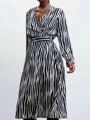 Omlottklänning - MANGO - Snygg omlottklänning med zebramönster i svart och vitt. Klänningen har lång ärm, v-ringning och knyt i midjan för en smickrande passform. Tillverkad i ett glansigt material som ger en lyxig känsla.