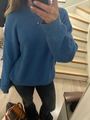 Blå stickad tröja med rund hals - En enkel och snygg blå stickad tröja med rund hals och långa ärmar. Tröjan har ribbstickade muddar vid ärmslut och nederkant. Perfekt för att hålla sig varm under kyliga dagar. Materialet ser ut att vara mjukt och bekvämt.