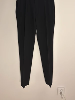 Svarta slim fit kostymbyxor H&M - Säljer ett par svarta kostymbyxor från H&M i slim fit-modell. Byxorna har en klassisk rak passform med pressveck och är perfekta för en clean och stilren look. Materialet känns mjukt och följsamt. Midjan är normalhög och benen är smala hela vägen ner.