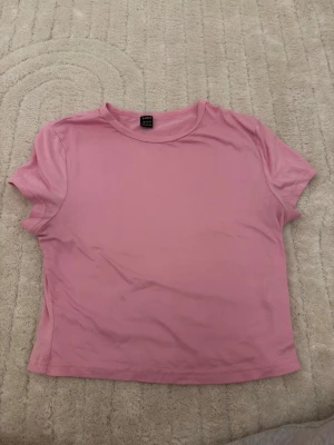 Rosa croppad t-shirt - En enkel och stilren rosa croppad t-shirt.. T-shirten har korta ärmar, rund halsringning och är tillverkad i mjuk bomull. Perfekt för en avslappnad och trendig look.