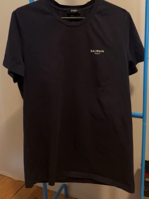 Svart t-shirt från Balmain Paris - Snygg svart t-shirt från Balmain Paris med diskret logga på bröstet. Klassisk rund halsringning och korta ärmar. Tillverkad i mjuk bomull som känns skön mot huden. Perfekt för en clean och stilren look. Storlek M