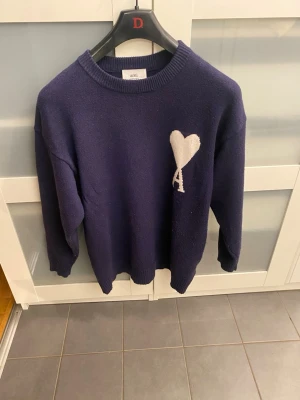 Mörkblå stickad tröja från Ami - Säljer en mörkblå stickad tröja från Ami med ett vitt hjärta och bokstaven 'A' broderat på bröstet. Tröjan har rund halsringning, långa ärmar och ribbade muddar vid ärmslut och nederkant. Perfekt för dig som gillar stilrena detaljer. SKRIV VIA DM OM DU ÄR INTRESSERAD PRIS KAN DISKUTERAS 