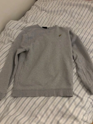 Grå sweatshirt från Lyle & Scott - Säljer en stilren grå sweatshirt från Lyle & Scott med deras klassiska guldfärgade logga broderad på bröstet. Tröjan har rund halsringning, långa ärmar och är gjord i mjukt sweatshirtmaterial. Perfekt basplagg till garderoben. lappen är avklippt tyvärr.