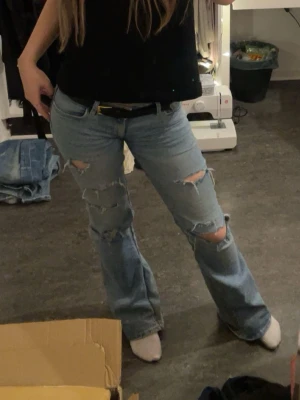 Ljusblå slitna bootcut jeans - Säljer ett par ljusblå bootcut jeans med flera slitningar + hål på framsidan.  Jeansen är lågmidjade, vilket jag gjort själv, det syns att de är sydda ( visas på bild ) men märks inte av så mycket. De är från Lindex. Storlek 158, men passar xs. Allt syns på bild. 