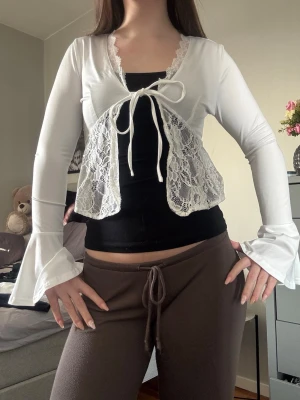 Vit spetsig bolerotopp med knyt - Söt vit bolerotopp med långa ärmar och volang vid ärmslut. Toppen har spetsdetaljer framtill och knytband vid bysten❤️