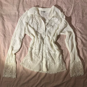 Vintage blus med spetsdetaljer - Säljer en krämvit blus med långärmad design, genomskinligt material och dekorativa knappar! 🤍Jag köpte den i Depart.A.Mental, men använder den inte längre.