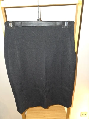 Svart pennkjol med dragkedja - Klassisk svart pennkjol med rak passform och dragkedja bak. Kjolen är knälång och har en stilren look som passar till många olika outfits. Tillverkad i ett mjukt material som känns bekvämt hela dagen.