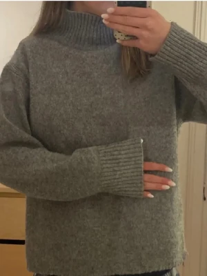 Grå stickad polotröja från zara - Jättefin grå stickad tröja med hög polokrage och långa ärmar. Tröjan har ribbstickade muddar vid ärmslut och nederkant, vilket ger en avslappnad och trendig look. Perfekt för kyliga dagar och enkel att matcha med jeans eller kjol.