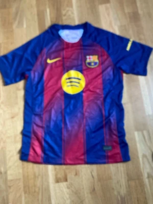 Barcelona matchtröja Nike röd/blå - Snygg FC Barcelona matchtröja från Nike i klassiska rödblå färger med gula detaljer. Tröjan har klubbmärke och Nike-logga på bröstet samt Spotify som sponsor framtill. Tillverkad i lätt och ventilerande funktionsmaterial, perfekt för fotbollsträning.