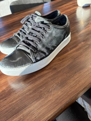 Svarta lanvins - Svarta sneakers med lågt skaft och vit sula. Ovandelen är i textil och syntet med svarta skosnören och metallöljetter. Tåpartiet är förstärkt i blankt material för en cool kontrast. Perfekta för en avslappnad streetstil.