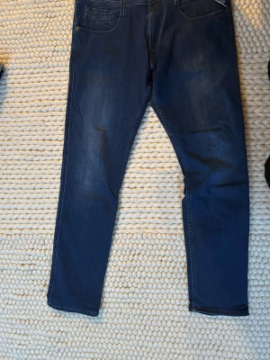 Mörkblå jeans från Replay Anbass - Snygga mörkblå jeans från Replay, modell Anbass. Klassisk femficksdesign med raka ben och diskreta slitningar framtill. Tillverkade i mjukt denimtyg som ger en bekväm passform. Perfekta för dig som gillar stilrena och tidlösa jeans. 