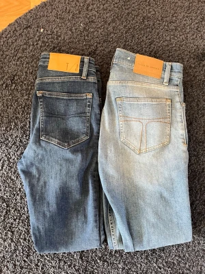 Två par jeans från T/J och Tiger of Sweden - Säljer två par jeans, ett par i mörkblå tvätt från T/J och ett par i ljusblå tvätt från Tiger of Sweden. Båda har klassisk femficksdesign, raka ben och läderpatch bak i midjan. Perfekta för en avslappnad och trendig look.