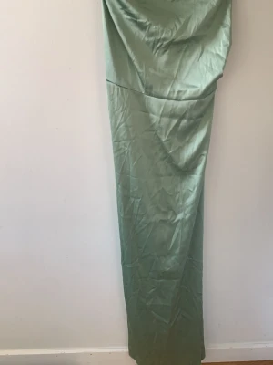 Grön långklänning i satin - Snygg grön långklänning i satin med enkel och elegant design. Klänningen har en rak passform och är axelbandslös, vilket ger en stilren look. Perfekt för dig som vill ha en minimalistisk och trendig outfit.