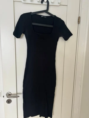 Svart kortärmad klänning Zara - En enkel och stilren svart klänning från Zara med korta ärmar och fyrkantig ringning. Klänningen är figurnära och har en klassisk, rak passform som passar till många olika tillfällen. Tillverkad i mjukt och stretchigt material.