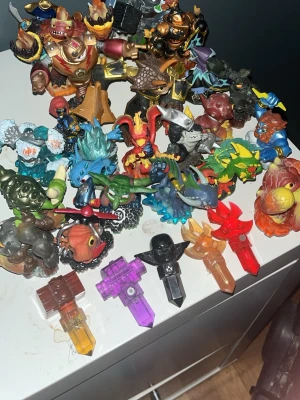 Skylanders-figurer och fällor - Samling med färgglada Skylanders-figurer och fällor i plast. Figurerna föreställer olika monster, drakar och robotar i flera färger som röd, blå, grön och gul. Fällorna är genomskinliga i rött, lila, svart, orange och brunt. Perfekt till Skylanders-spel och samling.