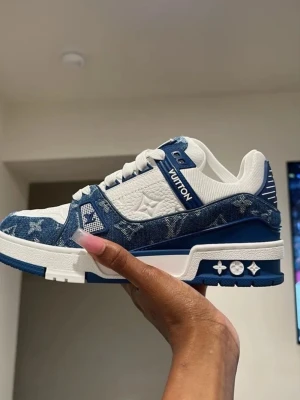 Louis Vuitton LV Trainer sneakers - Säljer Louis Vuitton LV Trainer sneakers i två färger: blå/vit och svart/vit. Skorna har klassisk låg siluett, LV-logga på sidan, och detaljer i denim med monogrammönster. Ovandelen är i läder och textil, med robust sula och snygga kontrastdetaljer.