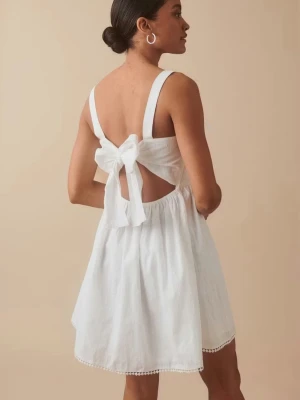 Vit kort klänning med rosett - Söt vit kortklänning med breda axelband och stor rosett i ryggen. Klänningen har öppen rygg. Aldrig använd och prislappen är fortfarande kvar!🌟