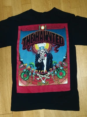 The Haunted (år 2009) T-Shirt | S / Small | Retro Y2K - T-Shirt med The Haunted (år 2009) tryck på framsidan (litet tryck) och baksidan (stort tryck)  Anvil. Small (Mått finns på bilderna!) 100% bomull.  Se bilder.