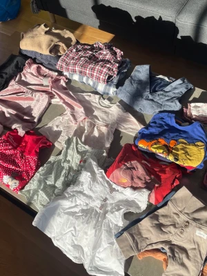 Stort klädpaket barn, mixade plagg - Säljer ett stort klädpaket med blandade barnkläder i olika färger och stilar. Paketet innehåller bland annat klänningar, skjortor, tröjor och bodys med motiv, rutigt, spets och volanger. Färgerna är blandade med rött, vitt, blått, beige och grått. Perfekt för dig som vill ha variation!