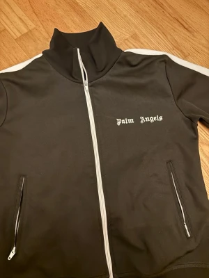 Äkta Palm Angels - Palm Angels svart hoodie med vit dragkedja och vita ränder längs ärmarna. Tröjan har hög krage, två fickor med dragkedja. Priset kan diskuteras vid snabb affär! Äkta!